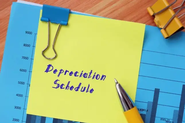 Graphs compiled on paper with a yellow Post-it note with the words Depreciation Schedule written on it.
