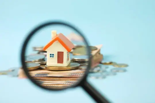 A magnifying glass highlighting a house sitting on top of a bunch of Australian currency.