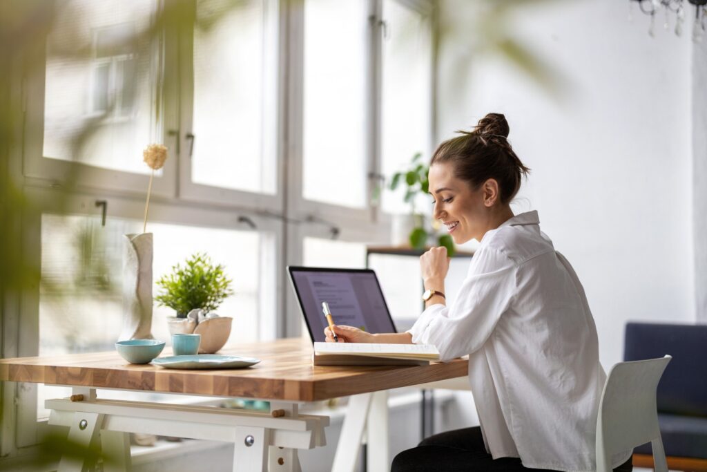Woman working at a home office desk with laptop and notebook, illustrating ATO home office expenses and she is reviewing her hours for the fixed rate method for work-from-home tax deductions.